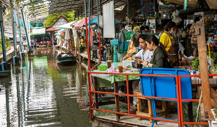 Couple mangeant à côté d'un bateau et de petites boutiques et restaurants au marché flottant de Bang Nam Phueng